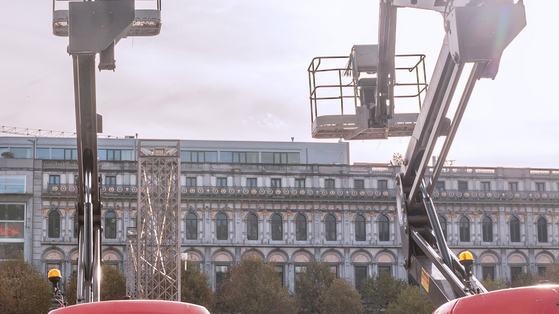 Two boom lifts are positioned in front of a grand building with an ornate facade and a modern extension.